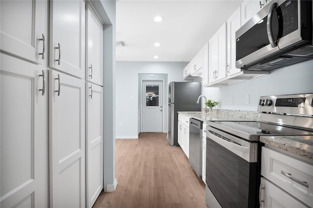 kitchen featuring appliances with stainless steel finishes, white cabinetry, light wood-style floors, and light stone countertops