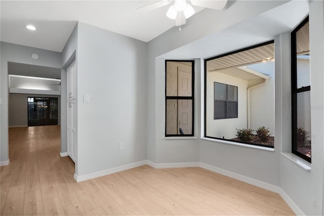 spare room with a healthy amount of sunlight, light wood-style flooring, baseboards, and ceiling fan