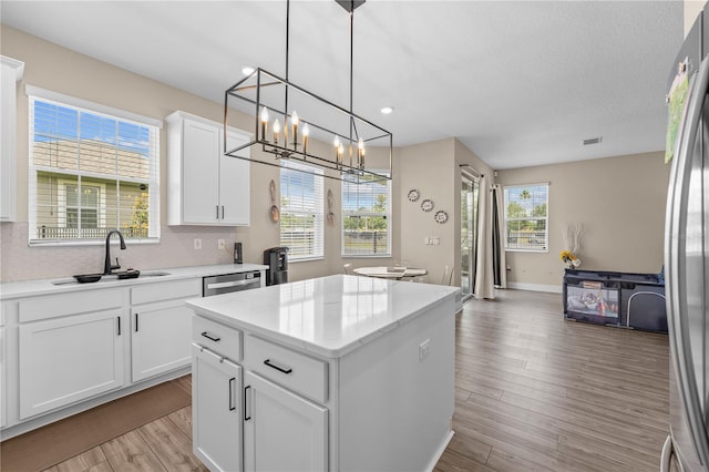 kitchen featuring appliances with stainless steel finishes, a kitchen island, white cabinets, light wood-type flooring, and pendant lighting