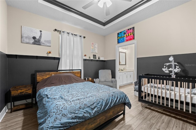 bedroom with ceiling fan with notable chandelier, ensuite bathroom, wood-type flooring, and a tray ceiling