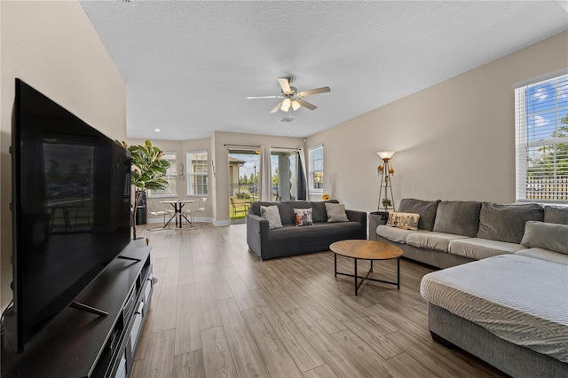 living room featuring plenty of natural light, ceiling fan, light wood-type flooring, and a textured ceiling