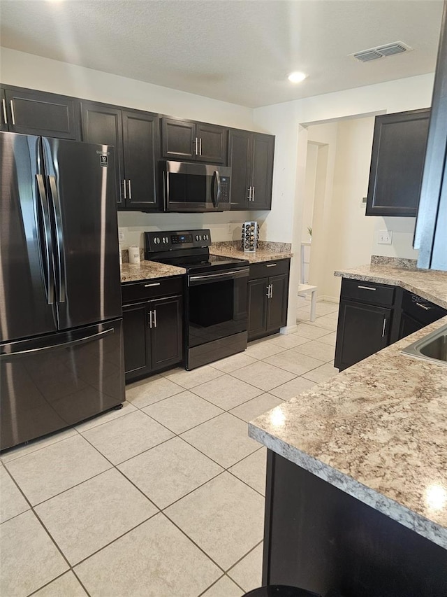 kitchen with appliances with stainless steel finishes, light tile floors, and light stone counters