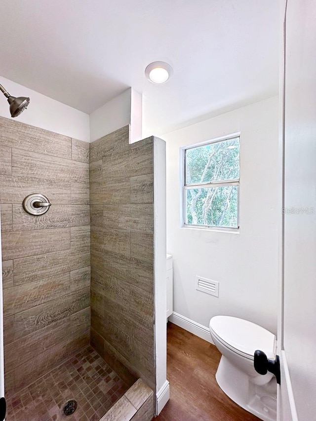 bathroom featuring hardwood / wood-style flooring, tiled shower, and toilet