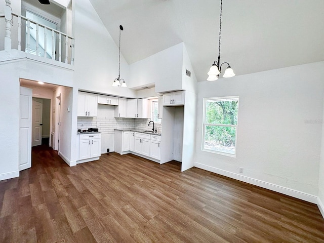 kitchen with tasteful backsplash, white cabinets, decorative light fixtures, high vaulted ceiling, and sink