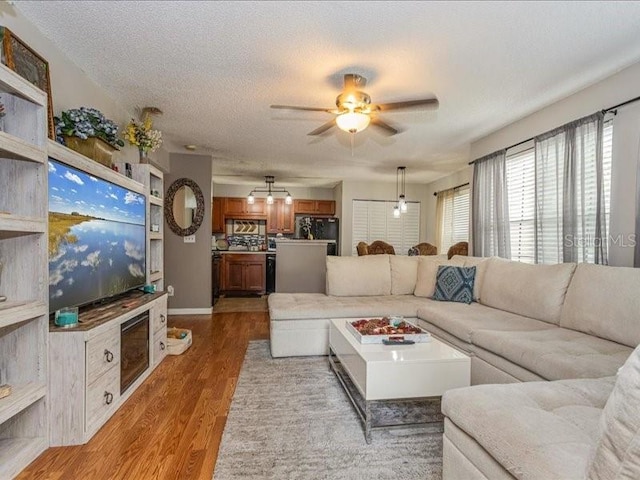 living room featuring light hardwood / wood-style floors, ceiling fan, and a textured ceiling