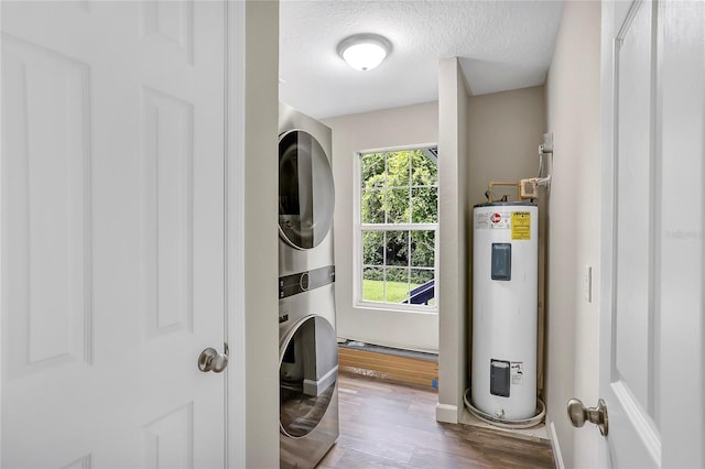 laundry room with water heater, hardwood / wood-style flooring, a wealth of natural light, and stacked washer / drying machine