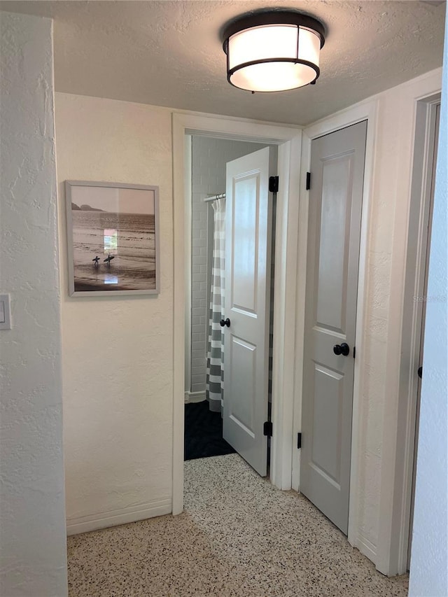 hall featuring light speckled floor, a textured wall, and a textured ceiling