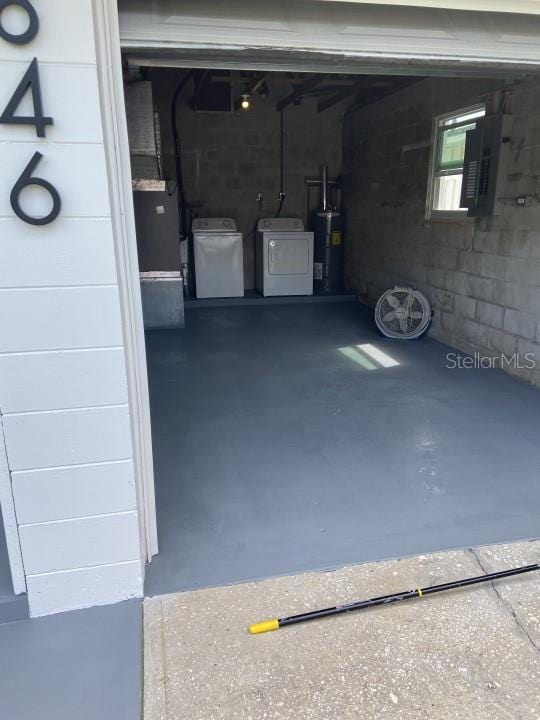 garage featuring water heater, washing machine and dryer, concrete block wall, and electric panel