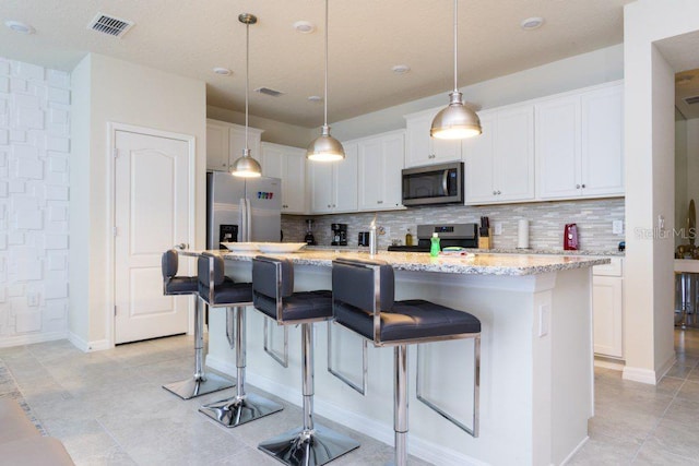 kitchen featuring hanging light fixtures, light tile flooring, stainless steel appliances, tasteful backsplash, and an island with sink