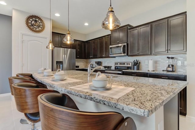 kitchen featuring decorative light fixtures, a kitchen bar, stainless steel appliances, tasteful backsplash, and light tile floors