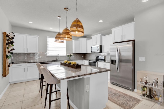 kitchen featuring stainless steel appliances, pendant lighting, dark stone countertops, white cabinets, and a kitchen island