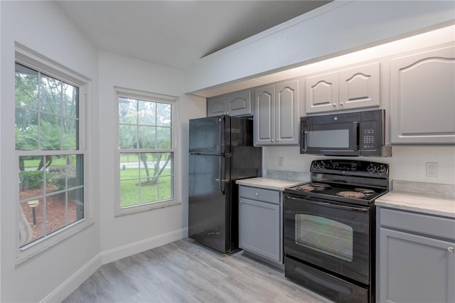 kitchen with gray cabinetry, black appliances, vaulted ceiling, and light hardwood / wood-style floors