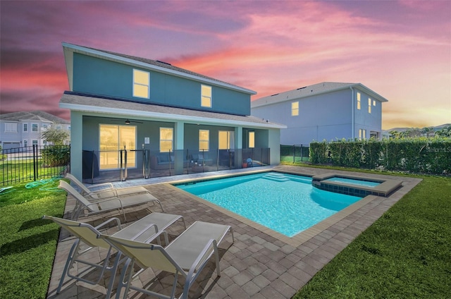 pool at dusk featuring a yard, an in ground hot tub, and a patio area