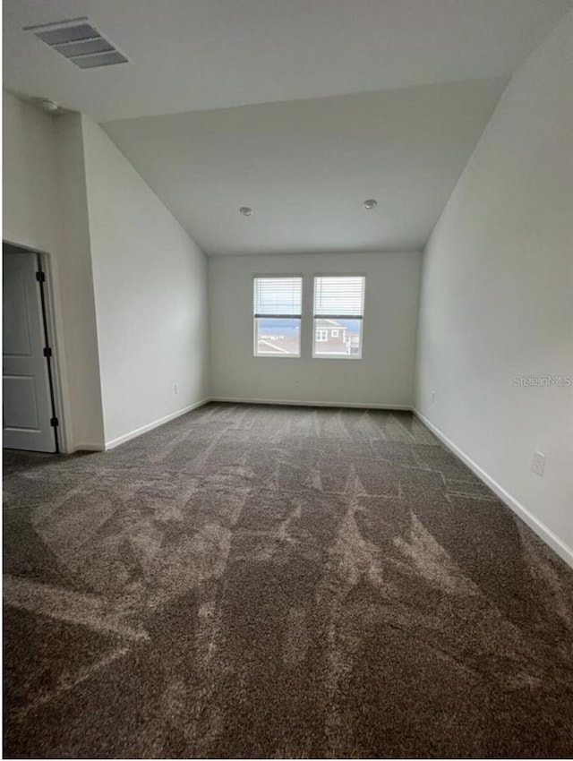 unfurnished room with dark colored carpet and lofted ceiling