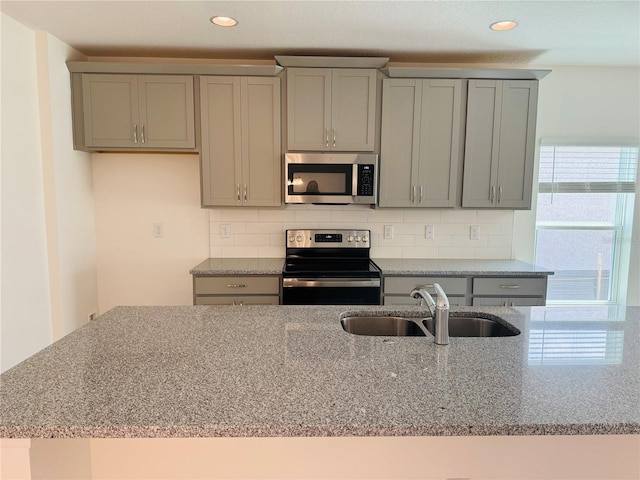 kitchen with gray cabinetry, stainless steel appliances, sink, light stone counters, and tasteful backsplash