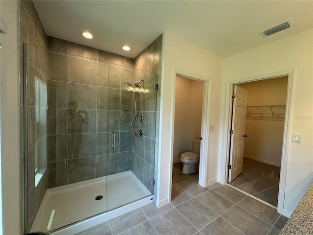 bathroom featuring toilet, tile floors, and a shower with shower door