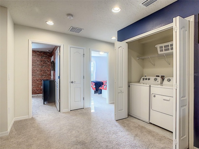 clothes washing area featuring a textured ceiling, washing machine and clothes dryer, light colored carpet, brick wall, and washer hookup