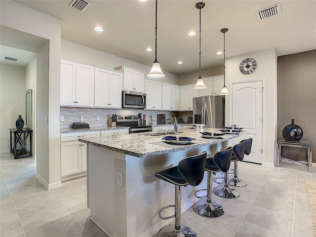 kitchen featuring a kitchen island with sink, decorative light fixtures, white cabinetry, appliances with stainless steel finishes, and light tile floors