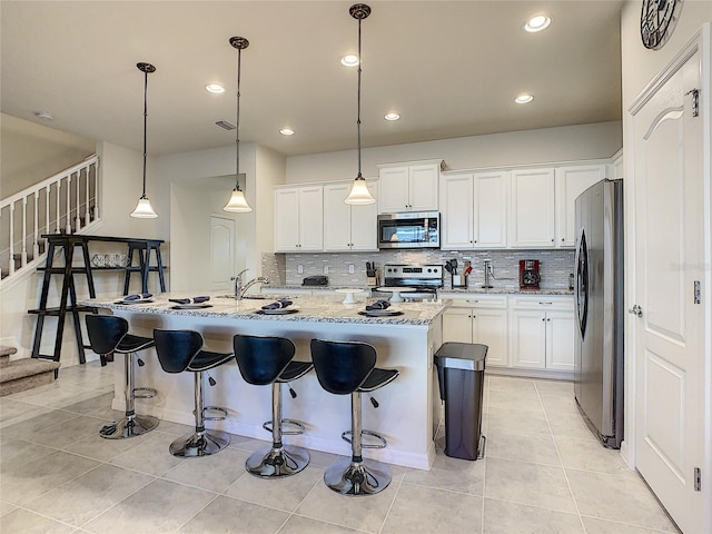 kitchen with appliances with stainless steel finishes, light tile floors, an island with sink, and decorative light fixtures