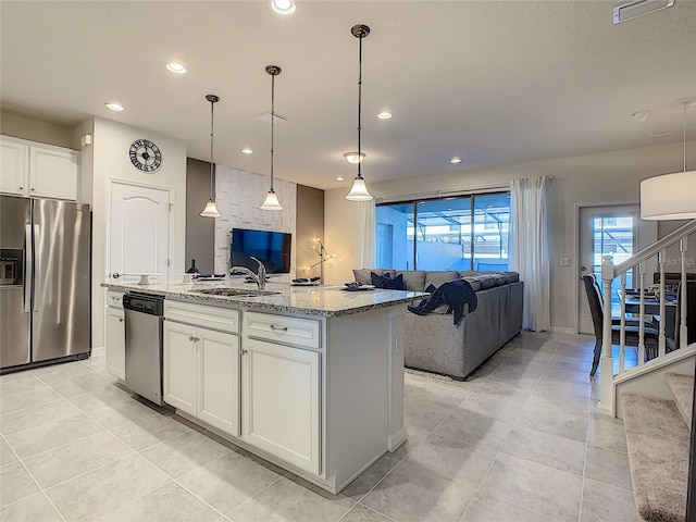 kitchen with light stone countertops, decorative light fixtures, appliances with stainless steel finishes, a center island with sink, and white cabinets