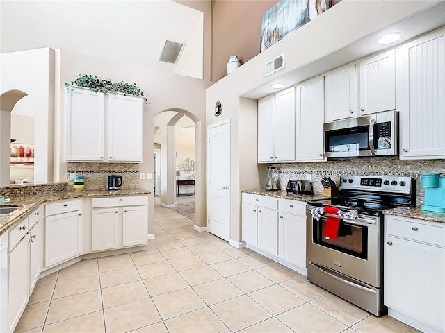 kitchen featuring light stone counters, light tile floors, white cabinets, tasteful backsplash, and stainless steel appliances