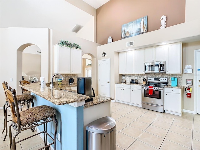 kitchen featuring backsplash, stainless steel appliances, white cabinets, and light stone countertops