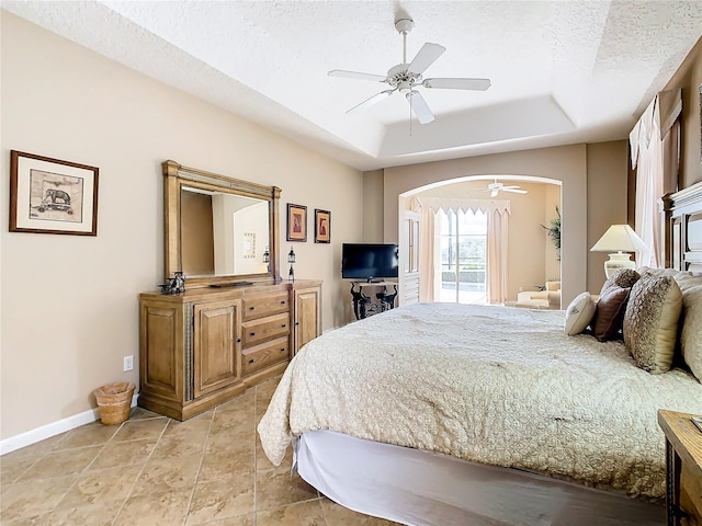 bedroom with a textured ceiling, a raised ceiling, ceiling fan, and tile floors