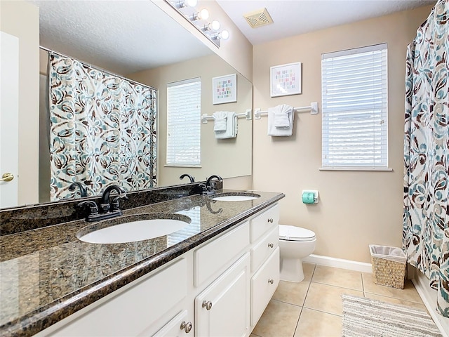 bathroom featuring large vanity, double sink, tile floors, toilet, and a healthy amount of sunlight