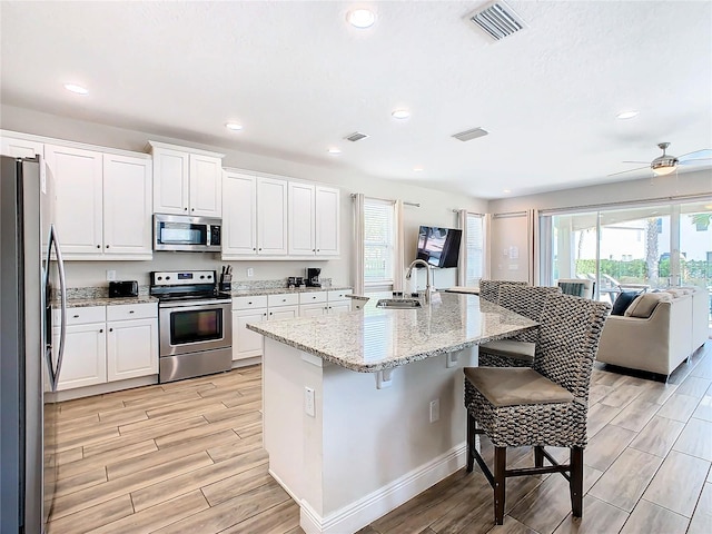 kitchen featuring stainless steel appliances, sink, a kitchen bar, a center island with sink, and ceiling fan