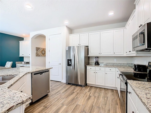 kitchen featuring white cabinets, appliances with stainless steel finishes, light wood-type flooring, and light stone countertops