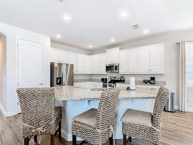 kitchen with white cabinets, a center island with sink, appliances with stainless steel finishes, and light stone countertops