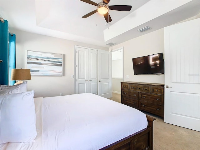 bedroom featuring light colored carpet, a closet, ceiling fan, and a raised ceiling