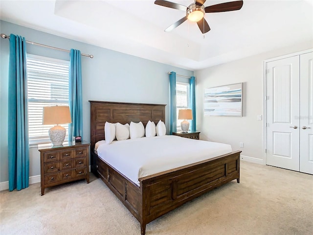 bedroom with light colored carpet, ceiling fan, a tray ceiling, and a closet