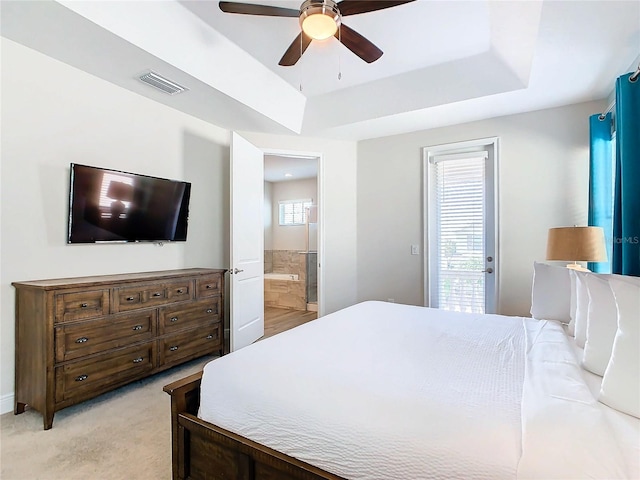 bedroom featuring ceiling fan, ensuite bathroom, access to exterior, a tray ceiling, and light colored carpet