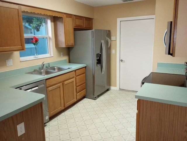 kitchen with brown cabinets, a sink, appliances with stainless steel finishes, light countertops, and light floors