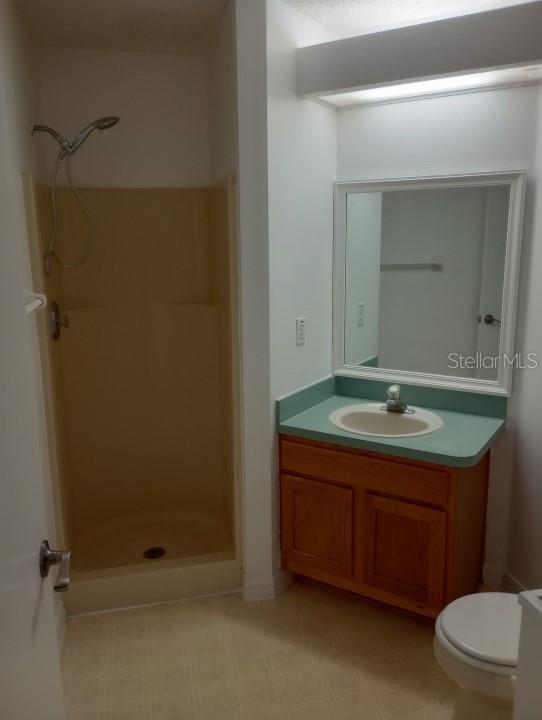 bathroom featuring walk in shower, tile flooring, vanity, and toilet