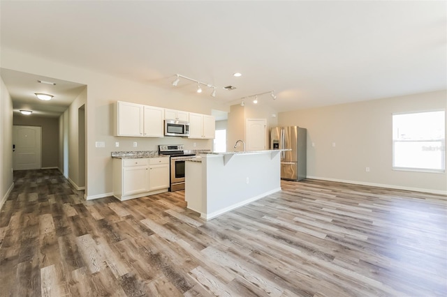 kitchen with white cabinets, stainless steel appliances, a center island with sink, light hardwood / wood-style floors, and track lighting