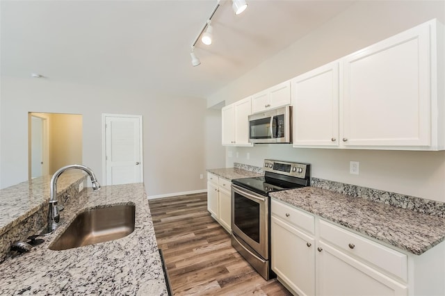 kitchen featuring light stone countertops, sink, stainless steel appliances, rail lighting, and hardwood / wood-style floors