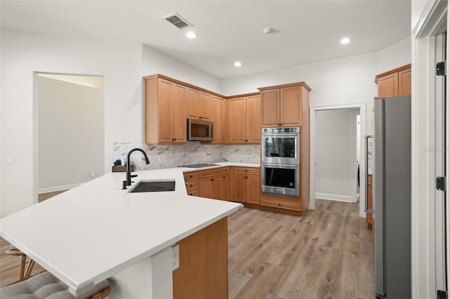 kitchen with kitchen peninsula, a breakfast bar, stainless steel appliances, sink, and light hardwood / wood-style floors