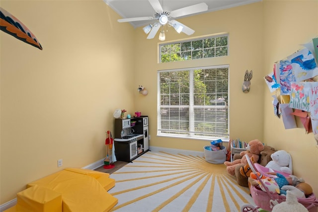 recreation room with ceiling fan, light carpet, a high ceiling, and ornamental molding