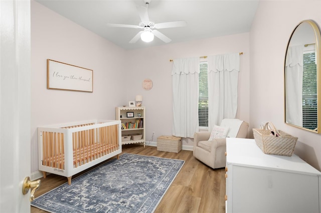 bedroom featuring ceiling fan, a nursery area, and light hardwood / wood-style floors