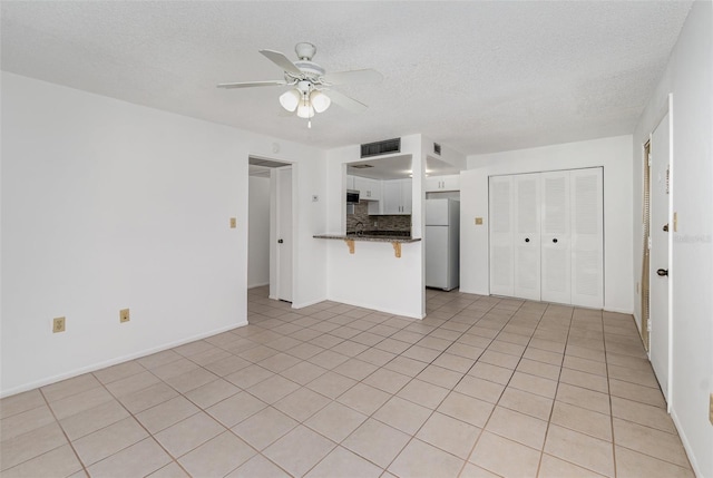 unfurnished living room with ceiling fan, light tile patterned floors, and a textured ceiling