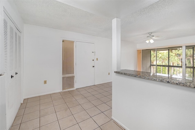 interior space with a textured ceiling, light tile patterned floors, stone countertops, and ceiling fan