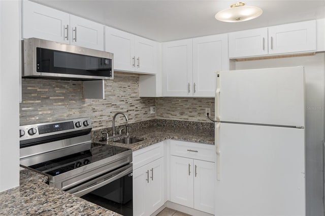 kitchen with stainless steel appliances, white cabinetry, dark stone countertops, and sink