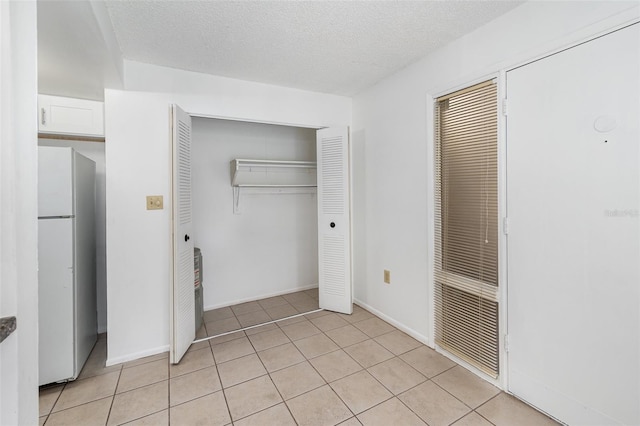 unfurnished bedroom featuring white refrigerator, light tile patterned floors, and a textured ceiling