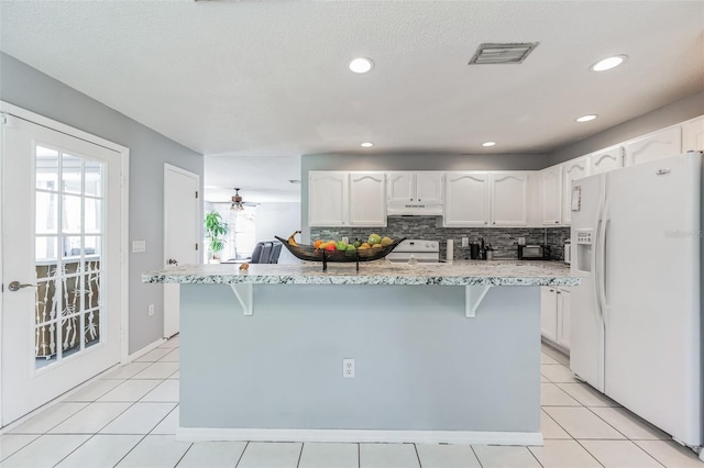 kitchen featuring white appliances, light tile floors, a breakfast bar area, and white cabinetry