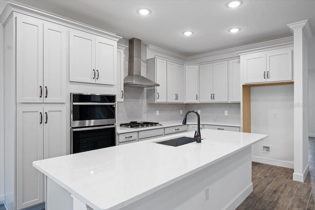 kitchen with wall chimney range hood, sink, appliances with stainless steel finishes, and a center island with sink