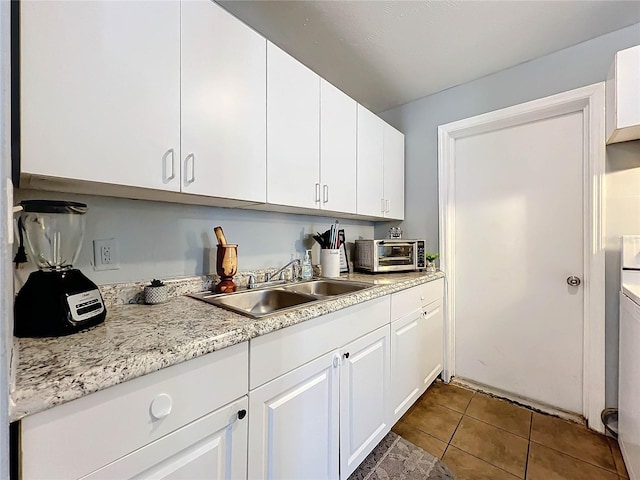 kitchen with tile patterned flooring, a toaster, a sink, white cabinetry, and light countertops