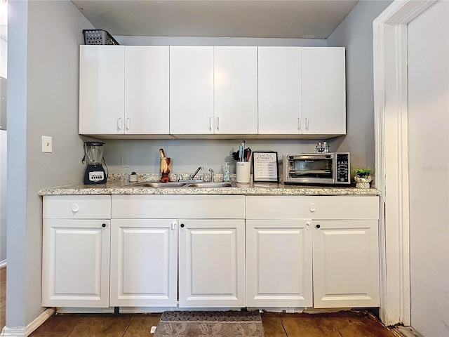 kitchen featuring a toaster, dark tile patterned flooring, light stone counters, white cabinetry, and a sink