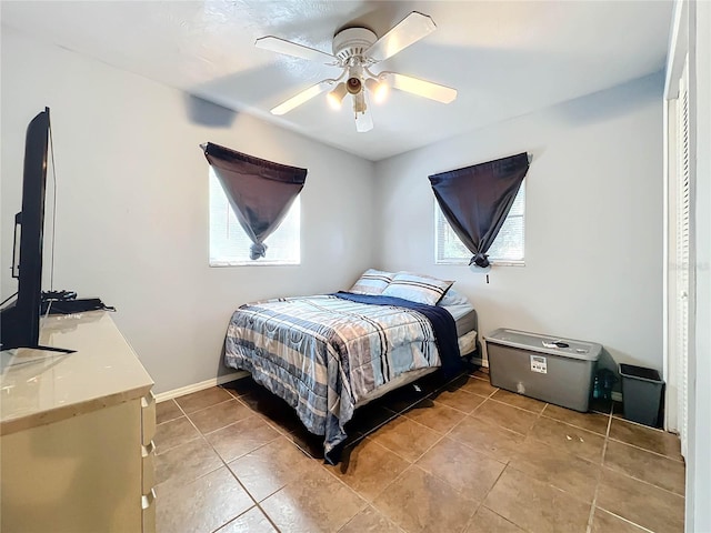 bedroom featuring a ceiling fan, multiple windows, baseboards, and light tile patterned flooring